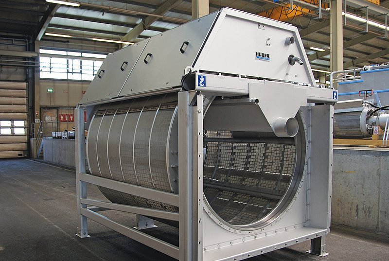 Large industrial drum screen in a factory setting, featuring a metal frame and mesh filter for processing materials.