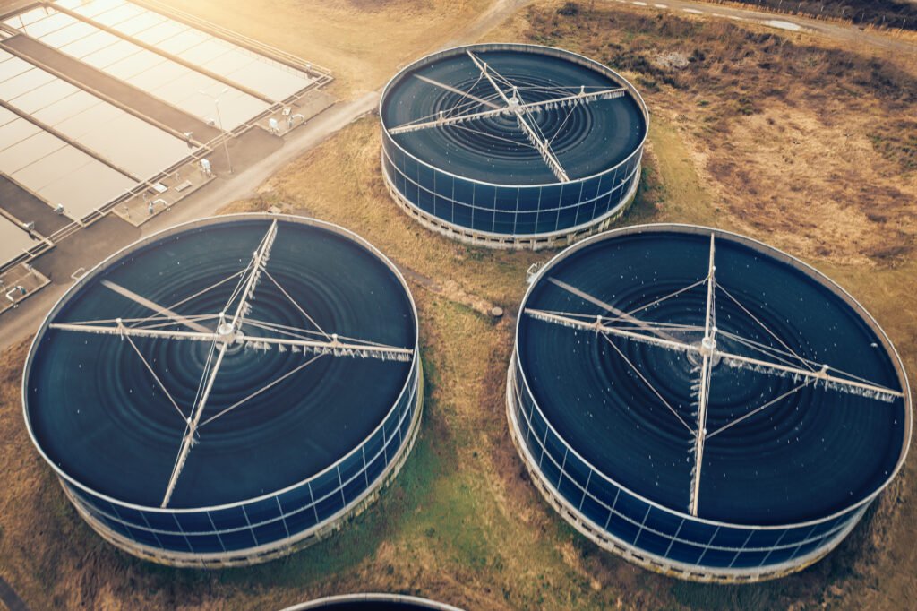 Aerial view of three large circular water treatment tanks and rectangular sedimentation basins at a wastewater facility.