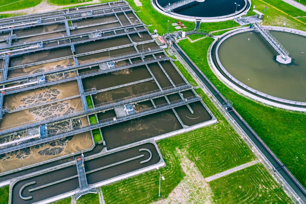 Aerial view of a wastewater treatment plant with clarifiers and aeration tanks surrounded by green grass.