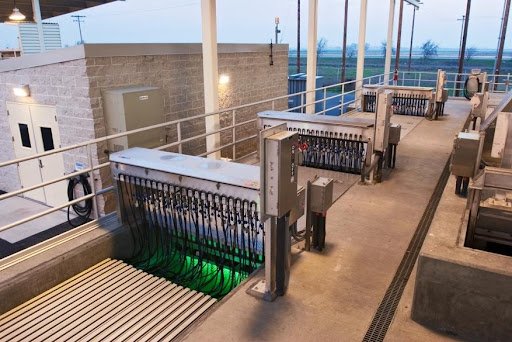 Industrial facility with machinery and control panels. Multiple cables and pipes are visible, with a glowing green light seen below grating. The setting appears to be a modern, clean, outdoor wastewater treatment area, showcasing impressive efficiency throughout its operations.