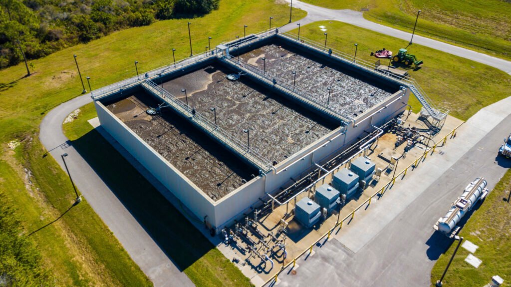 Aerial view of the expansive Eastern Water Reclamation Facility showcases three open tanks filled with water. The tanks are encircled by lush grassy areas and paved roads, with equipment and machinery strategically placed around the building, emphasizing efficient water reclamation.