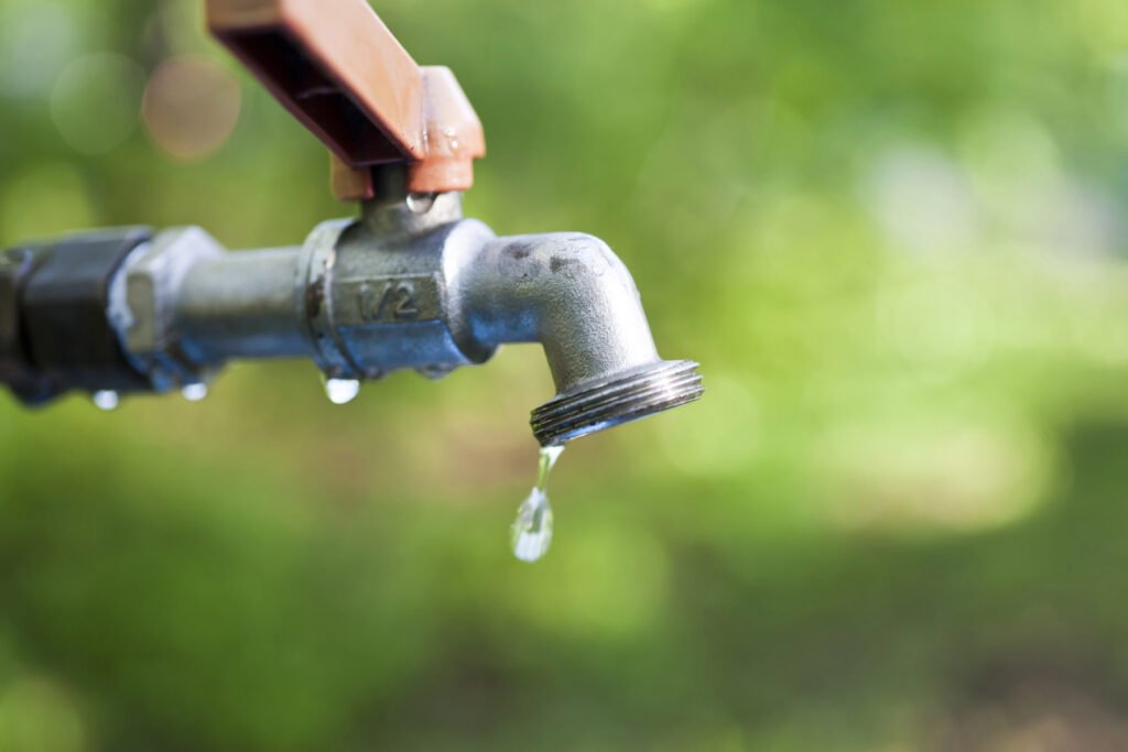 Dripping outdoor faucet with a blurred green background, capturing water waste.