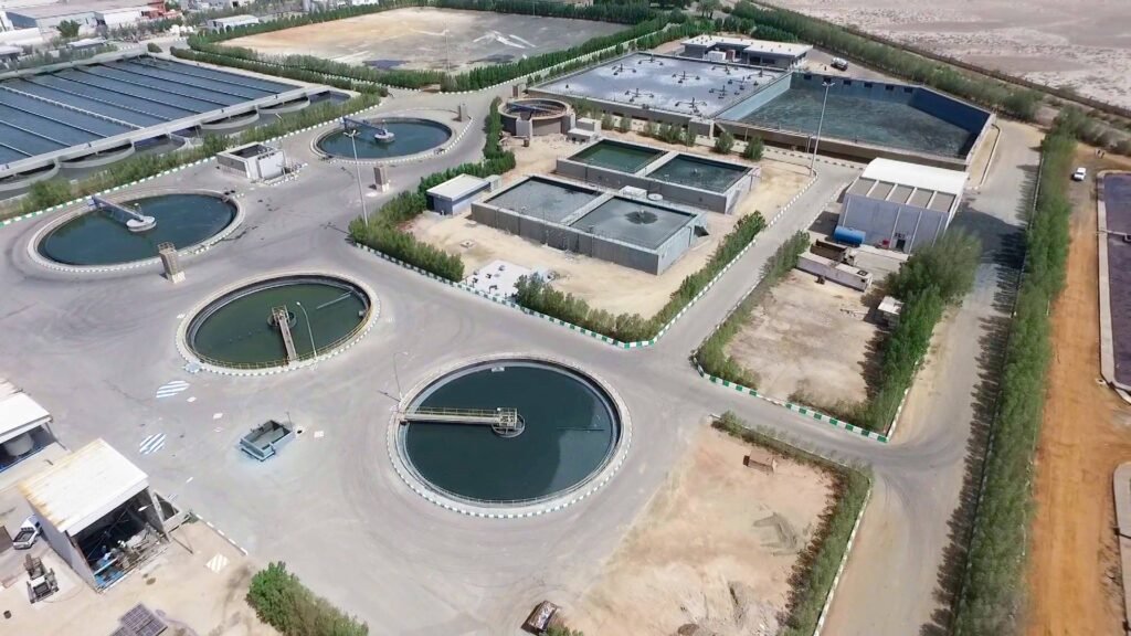 Aerial view of a large wastewater treatment plant showcases impressive infrastructure. Circular and rectangular tanks are visible, surrounded by roads and greenery. Buildings are scattered around the facility, set in a dry, open landscape, representing a robust future for sustainable water management.