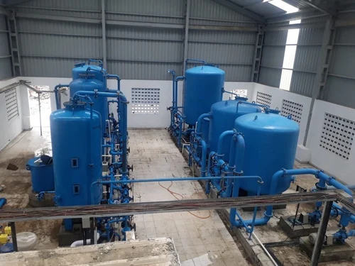 The interior of a large industrial facility showcases the demineralization process with multiple blue cylindrical tanks, utilizing the ion exchange method. These water treatment tanks are arranged in two rows inside a spacious, metal-roofed building.