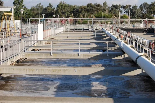 The Maynard C. Stiles Sewage Treatment Plant features large rectangular tanks, metal railings, and overhead pipes. These tanks are filled with partially treated water, with nearby trees and utility poles visible in the background, epitomizing Memphis North's dedication to environmental management.