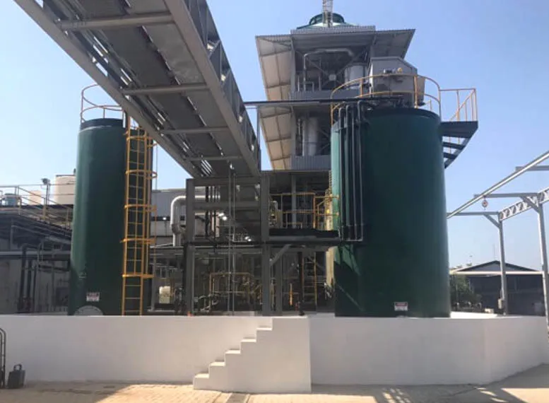 An industrial facility features large green cylindrical tanks and metal structures, likely housing Upflow Anaerobic Sludge Blanket Reactors. A walkway and stairs are visible in the foreground, amidst a network of pipes and ladders set against a clear blue sky.