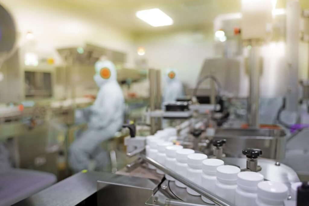 Scientists in protective gear work in a pharmaceutical lab with white bottles on a conveyor belt.