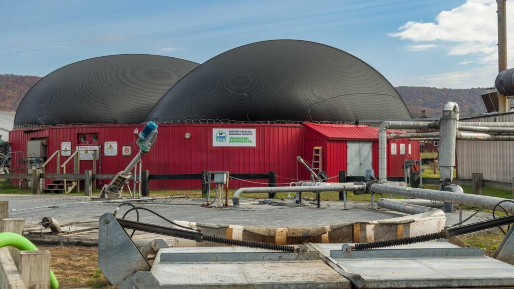 Red building with large domed roofs at Bar-Way Farm anaerobic digester facility, surrounded by industrial pipes and equipment.