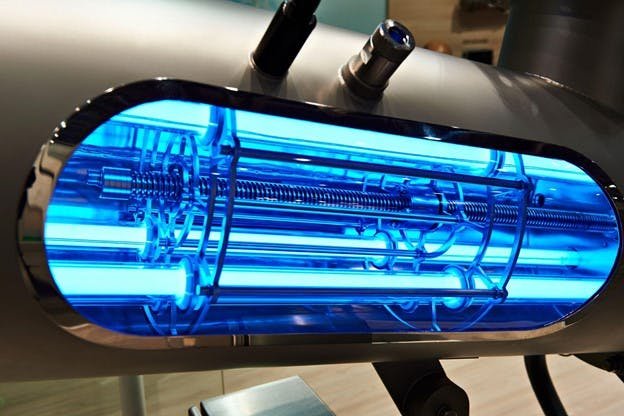 Close-up of a futuristic blue-lit machinery component with intricate metal rods and wires inside an oval casing.