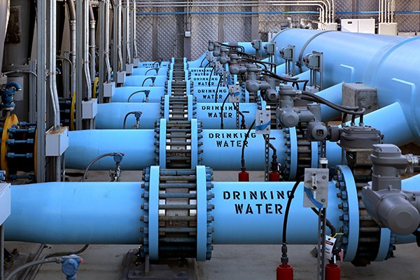 Blue pipes labeled "Drinking Water" in an industrial facility, arranged in parallel rows with valves and connectors.