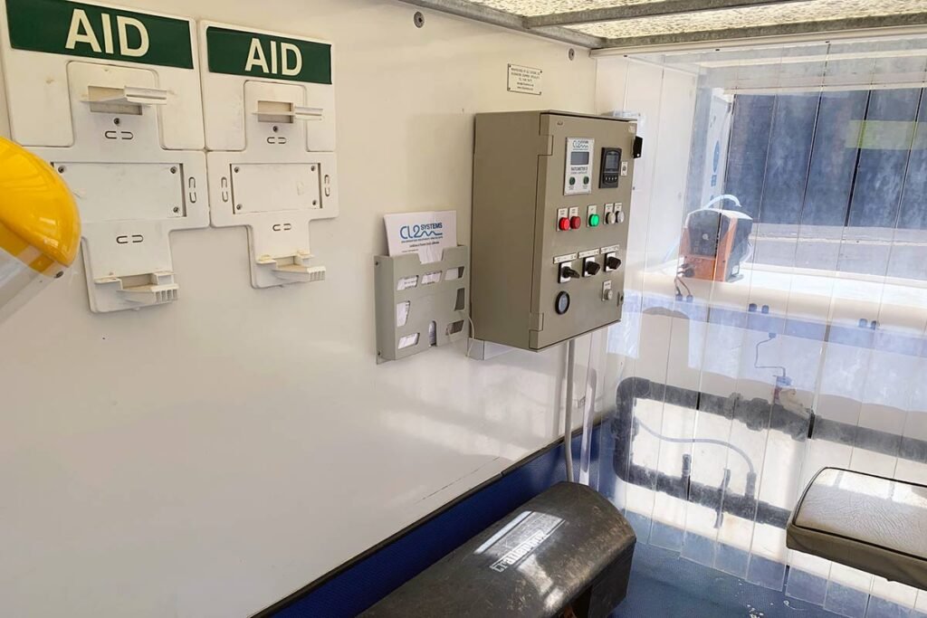 The interior of the station features wall-mounted aid boxes, a dechlorination system beside the electrical control panel, and a transparent divider. A cozy bench and a yellow helmet are visible as sunlight filters through the window.