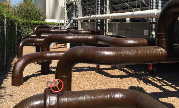 Large brown industrial pipes with red valve handles in a gravel-covered outdoor setting.