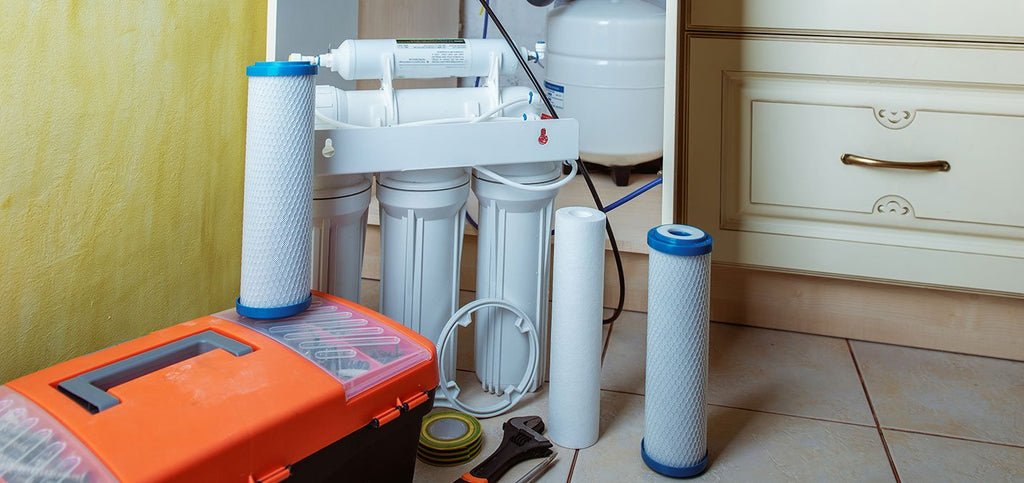 Home water filtration system installation with filters, tools, and a toolbox on the kitchen floor.