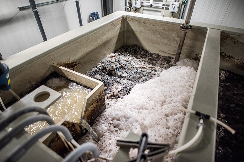 The industrial wastewater treatment tank, crucial for brewery wastewater treatment, contains frothy liquid and a metal stirring rod. It features multiple compartments and pipes for effective processing and separation. The clean and well-maintained environment highlights its commitment to innovative solutions.