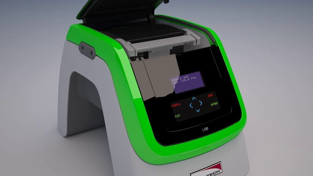 A compact green and gray COD Analyzer with an open lid reveals its interior. The front panel features a digital display showing several menu options for wastewater monitoring, along with a run button and navigation arrows, ideal for use in treatment plants.