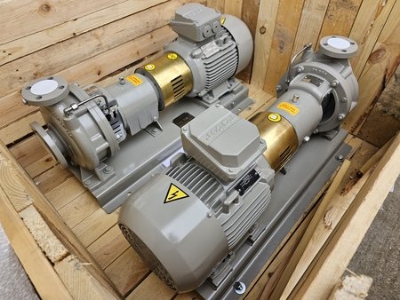 Two industrial transfer pumps with gray motors and golden cylindrical sections sit inside a wooden crate. They are oriented parallel to each other, featuring visible warning labels and electrical symbols, ensuring efficient liquid handling for various applications.